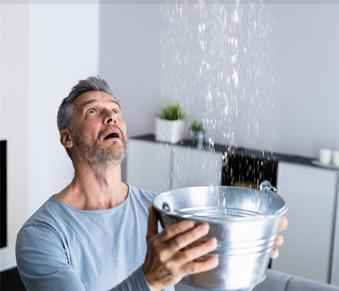 a man holding a tin bucket to catch water falling from his ceiling